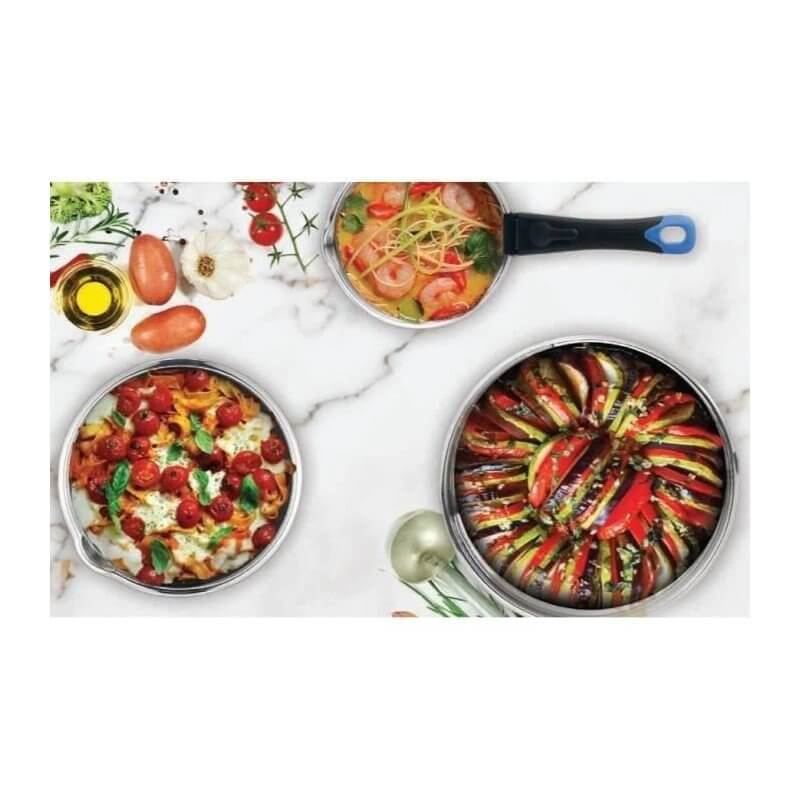 Ensemble de trois casseroles en acier inoxydable sur plan de travail blanc, garnies de plats colorés (pâtes, légumes) et huile d’olive autour.