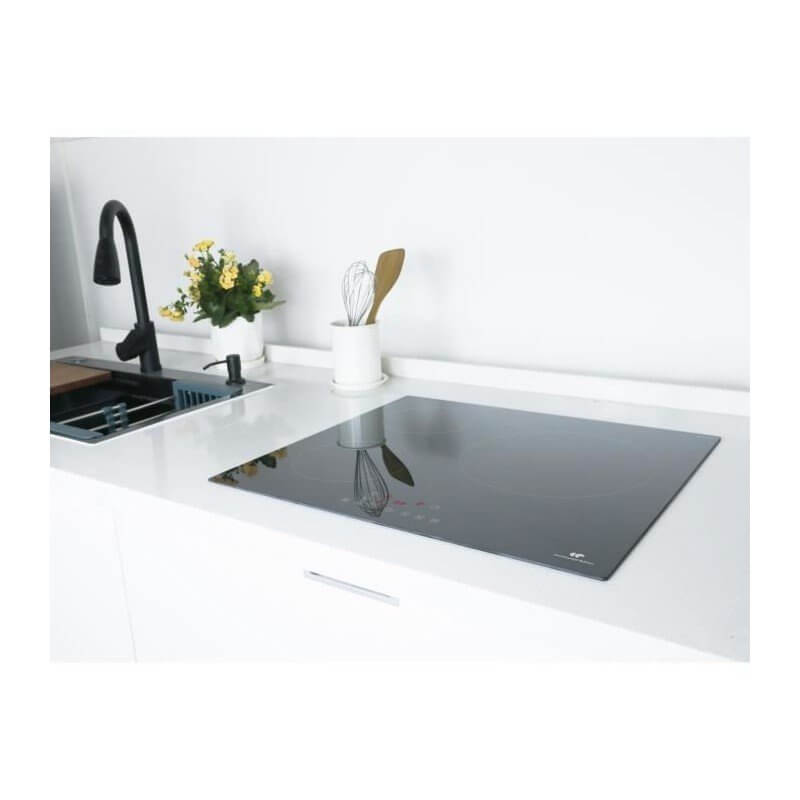 Table de cuisson à induction noire encastrée dans un plan de travail blanc, près d’un évier et d’un accessoire de cuisine. Alt: "Table de cuisson à induction noire sur plan blanc."