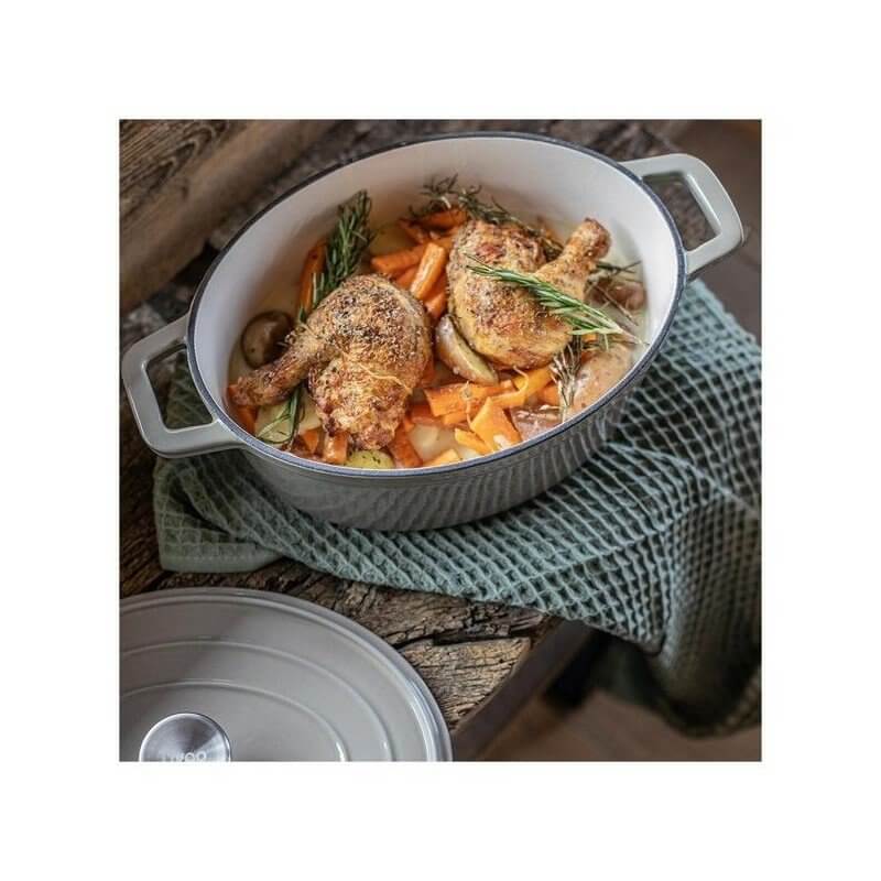 Plat mijoté avec cuisses de poulet rôties, légumes et herbes dans cocotte en fonte, sur planches en bois.