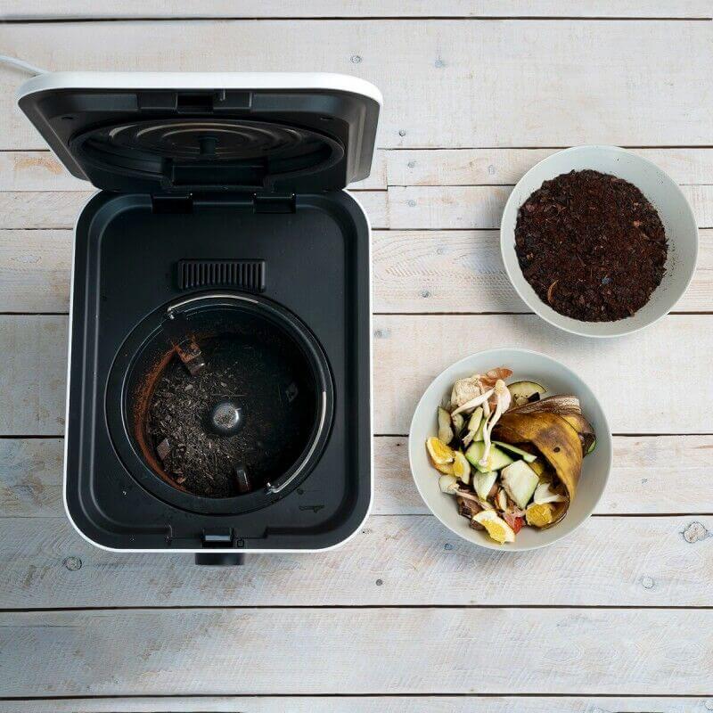 Petit appareil de cuisine (robot/Mixer) ouvert avec bol intérieur; à côté, deux bols contenant des déchets de cuisine et des épluchures/rejets de cuisson.