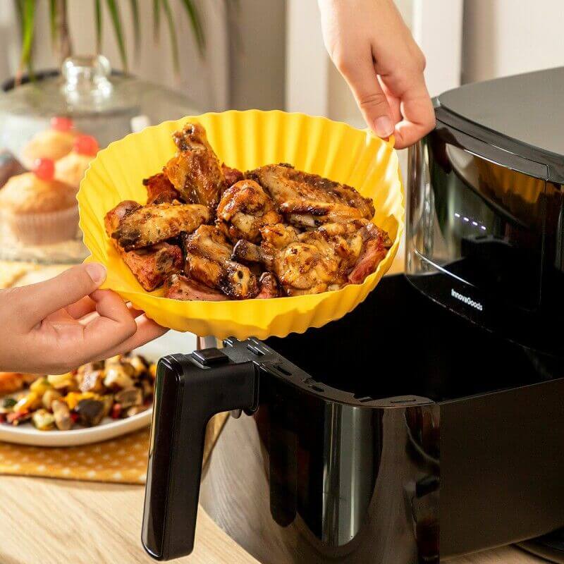 Personne plaçant dans un moule jaune des morceaux de viande cuits, sortant d’un air fryer noir sur un plan de cuisine.