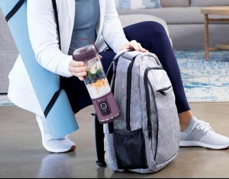 Personne assise avec un sac à dos gris et gourde portable; équipement de sport et tapis de yoga à proximité.