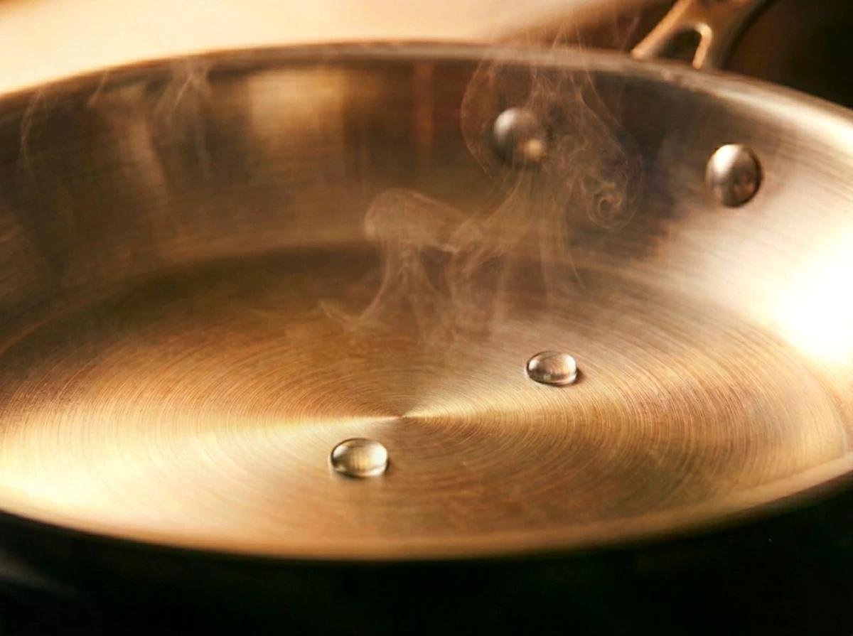 Poêle en cuivre brillant avec vapeur légère et vis apparentes, zoom sur la surface circulaire et les rivets.
