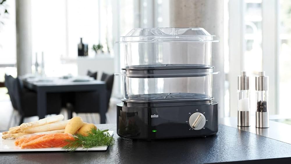 Robot multifonctions BRAUN avec paniers vapeur en verre sur la table, près de légumes et poissons fumée, dans une cuisine moderne.